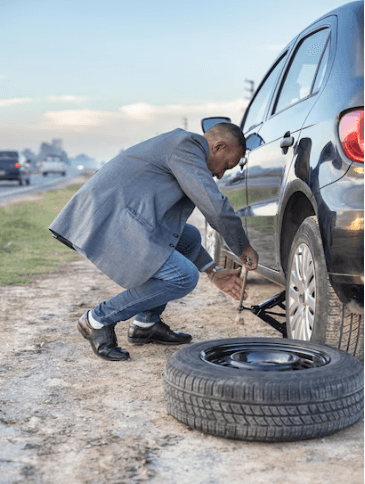 Man in business suit stranded on roadside changing a flat tire